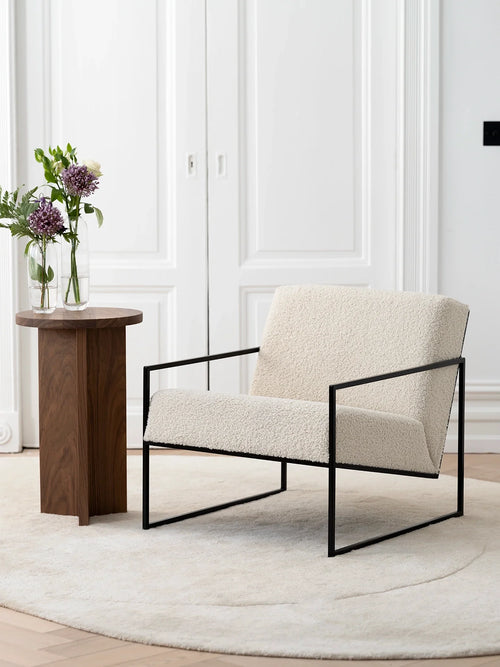 Armchair Kent – Black Frame – Ivory Bouclé Cushion in a minimalist interior setting with a side table and flowers.