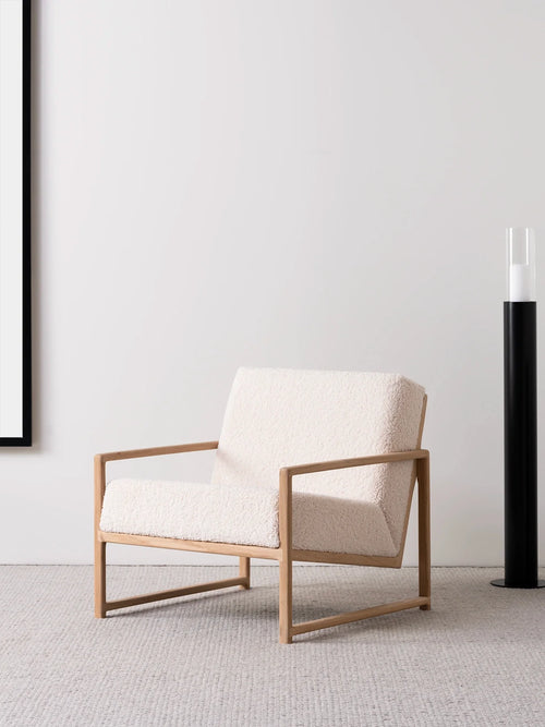 Armchair Einar with oak frame and ivory bouclé cushion in a modern living space setting.