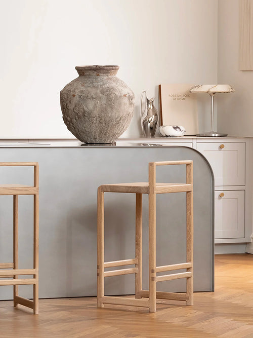 Minimalist Scandinavian kitchen with curved gray island and Ebba oak bar stools, styled with a textured ceramic vase and neutral decor.