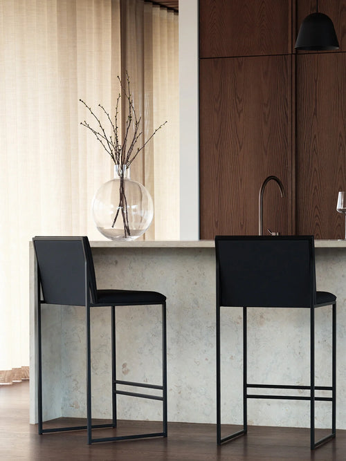 Modern kitchen interior with Philip black leather bar stools, dark wood cabinetry, stone island bench, and minimalist contemporary styling.